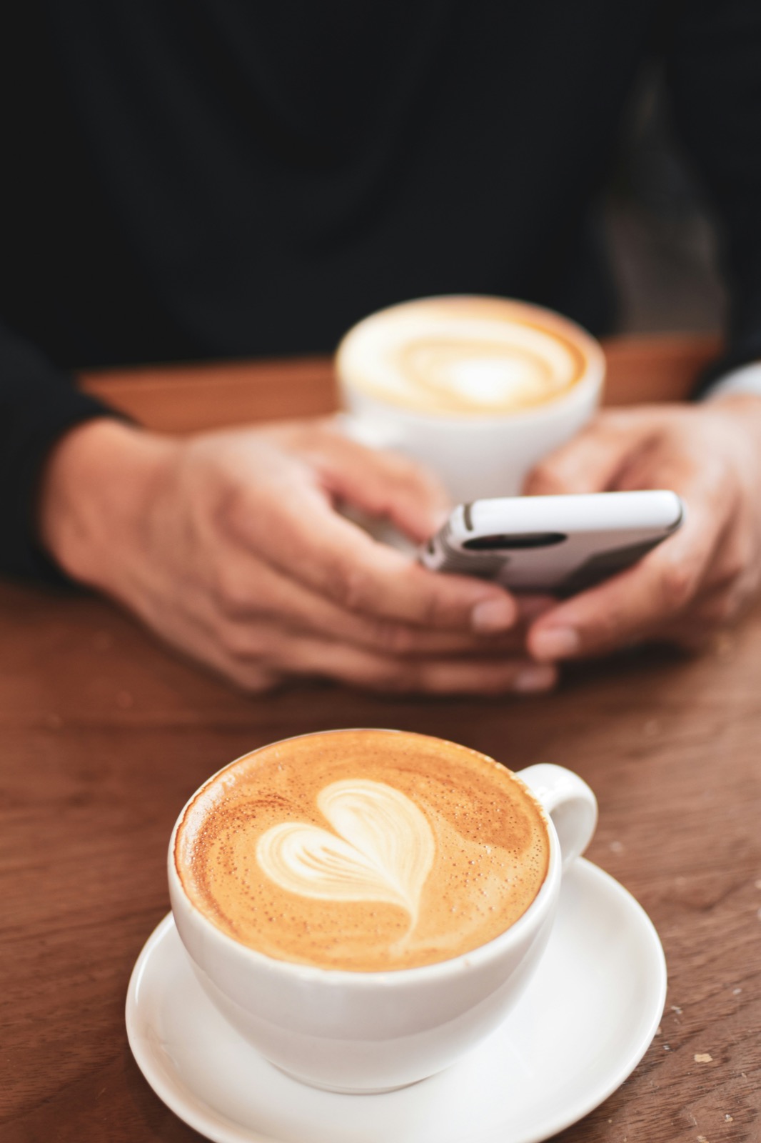 Persona escribiendo en su teléfono junto a una taza de café